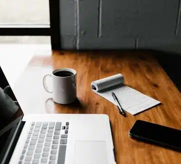 MacBook Pro, white ceramic mug,and black smartphone on table