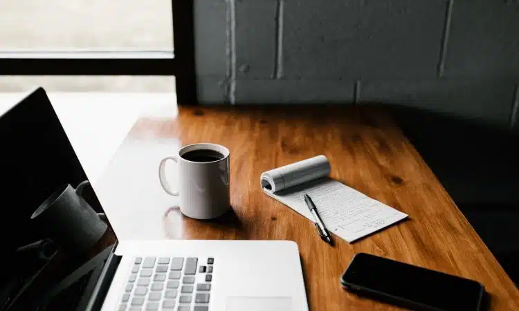 MacBook Pro, white ceramic mug,and black smartphone on table