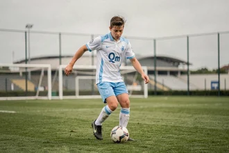 Jeune joueur de football en formation au centre d'entraînement de l'OM, dribblant sur un terrain professionnel